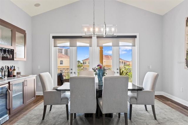 dining area with lofted ceiling, indoor bar, an inviting chandelier, hardwood / wood-style floors, and beverage cooler