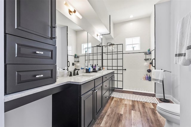 bathroom with a tile shower, dual bowl vanity, hardwood / wood-style floors, and toilet