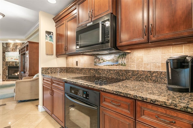 kitchen featuring ornamental molding, dark stone counters, black appliances, a tile fireplace, and light tile patterned floors