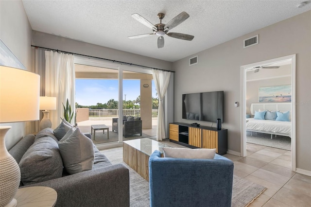 living room with ceiling fan, light tile patterned flooring, and a textured ceiling