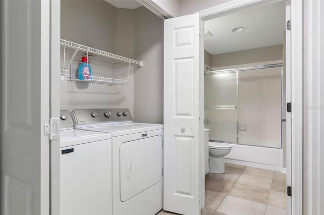 clothes washing area with a textured ceiling, washing machine and dryer, and light tile patterned flooring