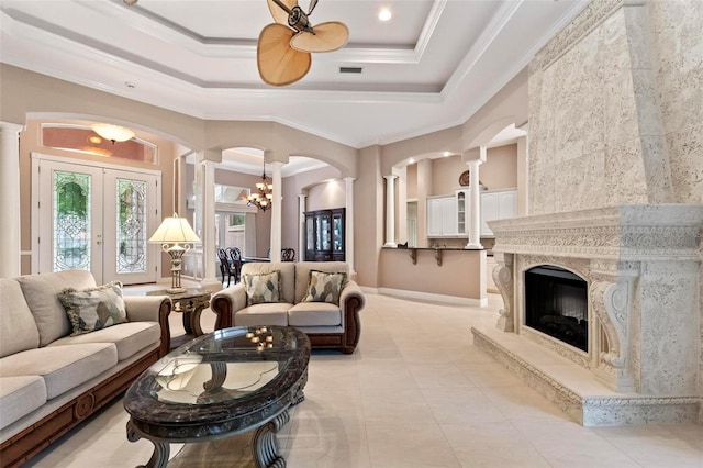 living room with french doors, ceiling fan with notable chandelier, a tray ceiling, crown molding, and a premium fireplace