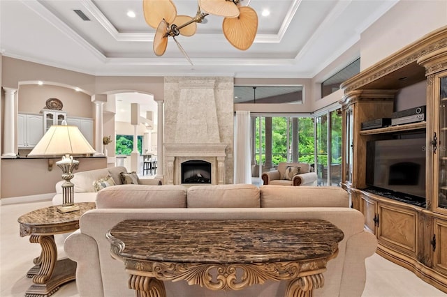 tiled living room featuring a tray ceiling, crown molding, a fireplace, and ceiling fan