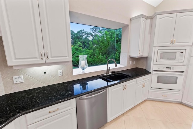 kitchen featuring decorative backsplash, dark stone counters, white appliances, sink, and white cabinetry