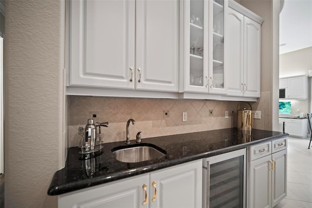 bar featuring tasteful backsplash, dark stone counters, beverage cooler, sink, and white cabinetry