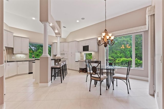 dining space featuring an inviting chandelier, ornate columns, light tile patterned floors, and vaulted ceiling