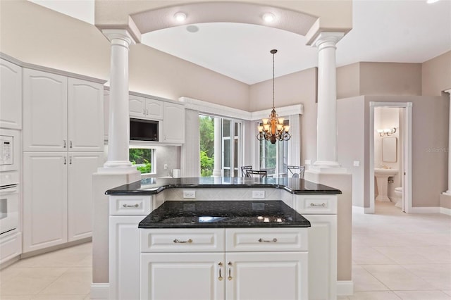 kitchen with ornate columns, white cabinetry, light tile patterned floors, and an inviting chandelier