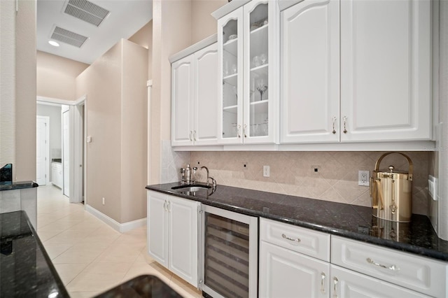 kitchen featuring dark stone counters, sink, light tile patterned flooring, white cabinetry, and beverage cooler