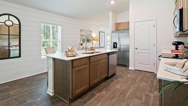 kitchen with wood walls, sink, an island with sink, and appliances with stainless steel finishes