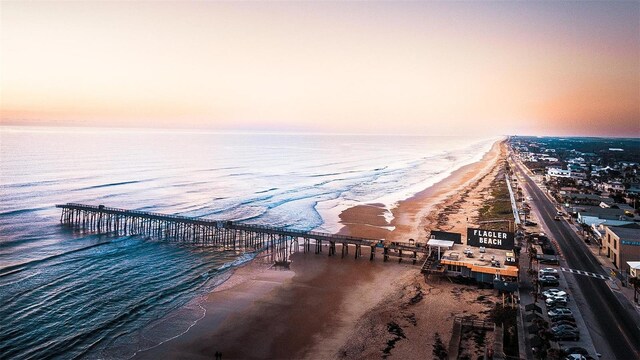 aerial view at dusk with a water view and a view of the beach