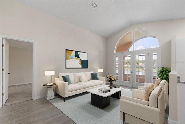 living room featuring vaulted ceiling, light hardwood / wood-style floors, french doors, and a textured ceiling