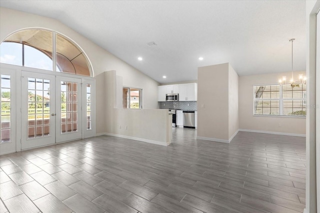 unfurnished living room featuring a notable chandelier, vaulted ceiling, dark hardwood / wood-style floors, and french doors