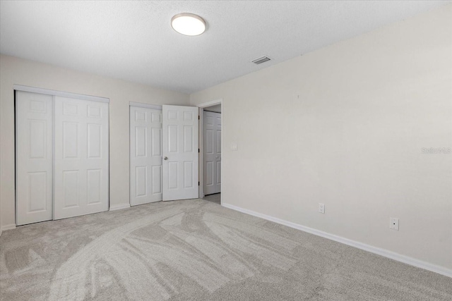 unfurnished bedroom featuring light carpet, a textured ceiling, and multiple closets