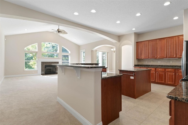 kitchen with a center island, lofted ceiling, light carpet, decorative backsplash, and dark stone counters