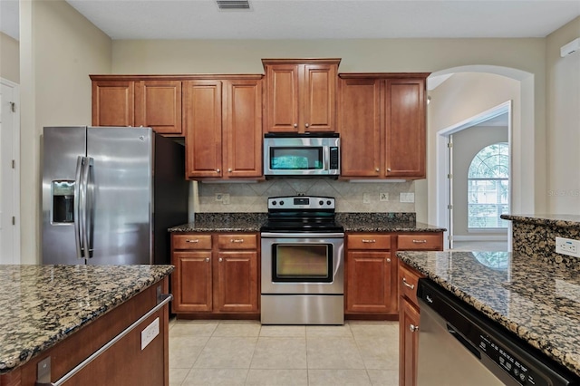 kitchen featuring dark stone counters, stainless steel appliances, backsplash, and light tile patterned floors