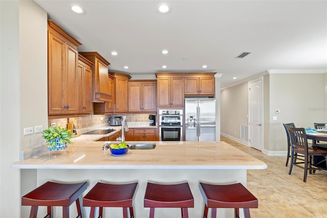 kitchen featuring sink, kitchen peninsula, decorative backsplash, a breakfast bar, and appliances with stainless steel finishes