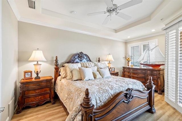 bedroom with light wood-type flooring, a tray ceiling, ceiling fan, and ornamental molding