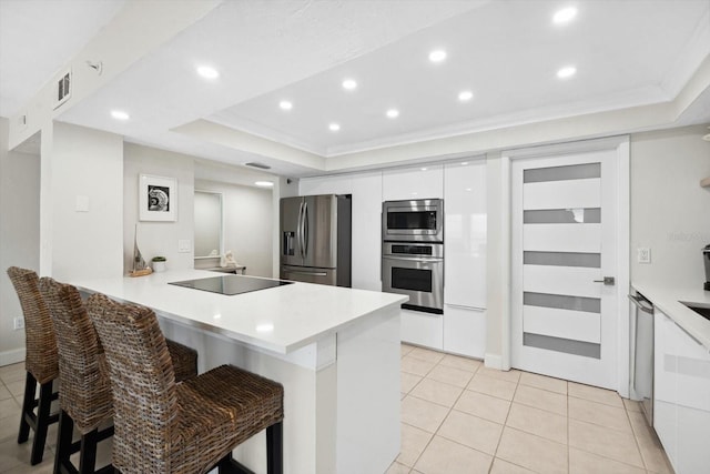 kitchen with a raised ceiling, a breakfast bar area, white cabinetry, kitchen peninsula, and stainless steel appliances