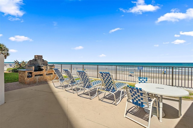 view of patio / terrace featuring a water view, a view of the beach, and an outdoor stone fireplace