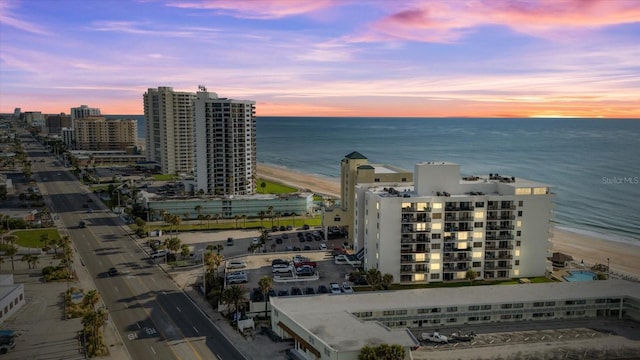 aerial view at dusk featuring a water view and a beach view