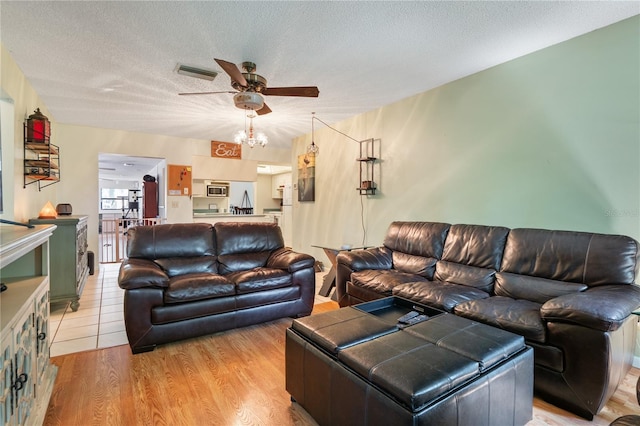 living room with ceiling fan, a textured ceiling, and light wood-type flooring