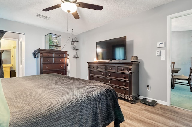 bedroom with ceiling fan, light hardwood / wood-style floors, a textured ceiling, and ensuite bathroom