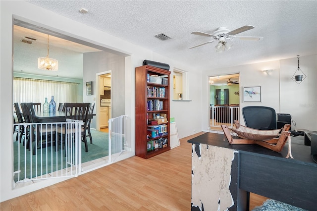 home office featuring ceiling fan with notable chandelier, a textured ceiling, and hardwood / wood-style flooring