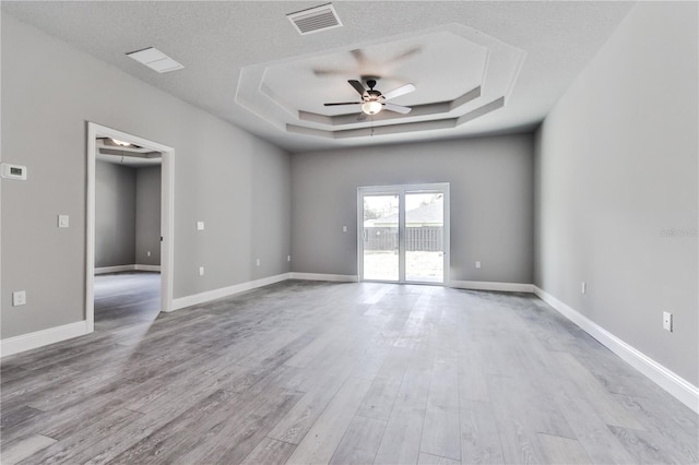 spare room with a textured ceiling, a raised ceiling, ceiling fan, and light wood-type flooring