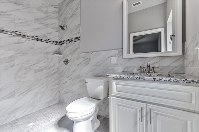 bathroom featuring vanity, a tile shower, tile walls, and toilet