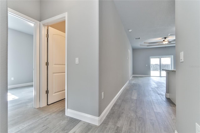 hallway featuring a tray ceiling and light hardwood / wood-style flooring