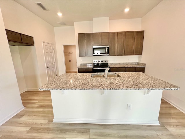 kitchen featuring a breakfast bar, light stone counters, a center island with sink, and appliances with stainless steel finishes