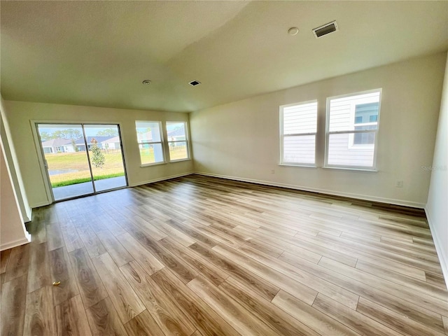 empty room featuring a healthy amount of sunlight, vaulted ceiling, and light hardwood / wood-style floors