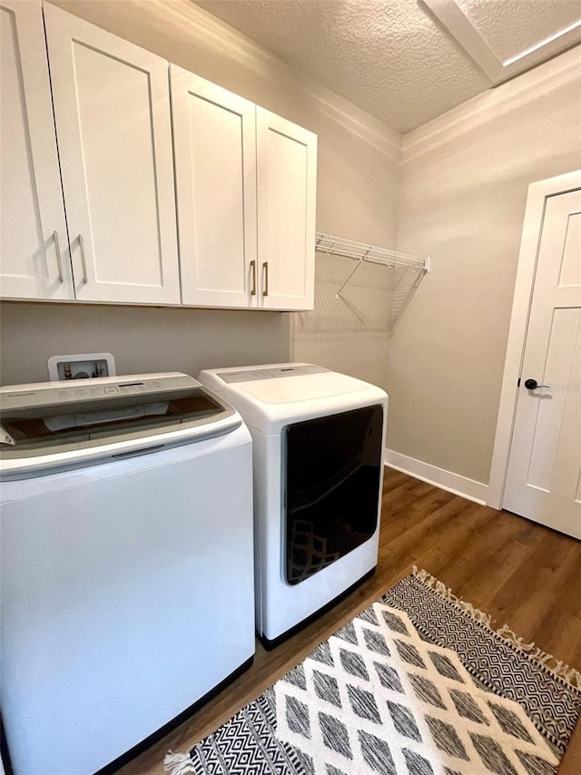 clothes washing area with cabinets, a textured ceiling, separate washer and dryer, and dark hardwood / wood-style floors