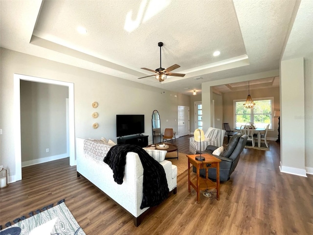 living room featuring a textured ceiling, dark hardwood / wood-style flooring, a tray ceiling, and ceiling fan