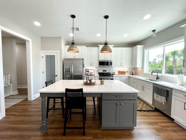 kitchen featuring stainless steel appliances, sink, a center island, gray cabinets, and hanging light fixtures