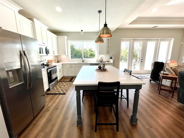 kitchen with french doors, dark wood-type flooring, stainless steel appliances, decorative light fixtures, and white cabinets