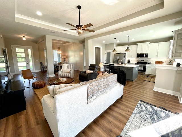 living room featuring sink, dark hardwood / wood-style floors, ceiling fan, a textured ceiling, and a tray ceiling