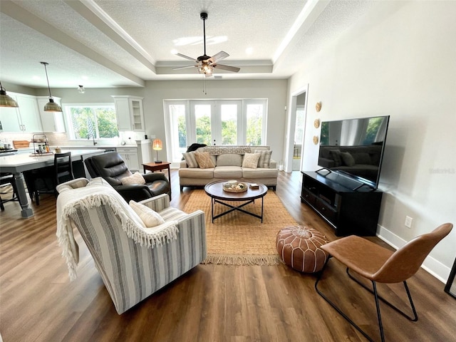 living room with a raised ceiling, ceiling fan, light hardwood / wood-style flooring, and a textured ceiling