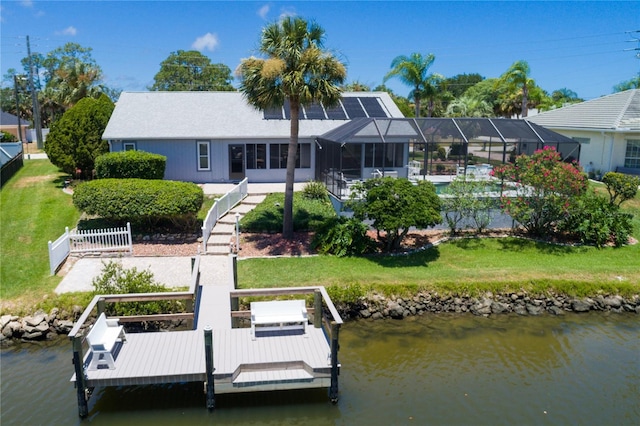 back of house with a water view, a lawn, fence, boat lift, and a lanai