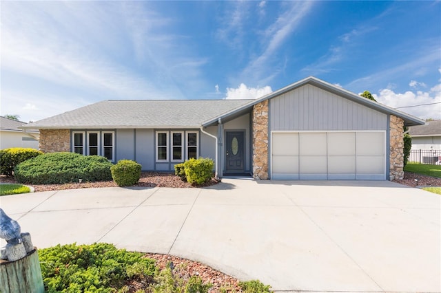 view of front of home with stone siding, an attached garage, concrete driveway, and fence