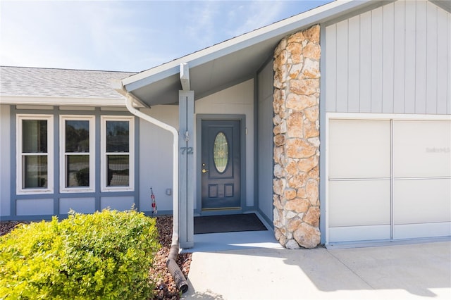 view of exterior entry featuring stone siding, a garage, and roof with shingles