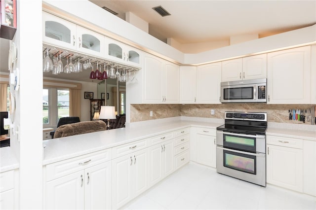 kitchen with visible vents, glass insert cabinets, light countertops, decorative backsplash, and stainless steel appliances