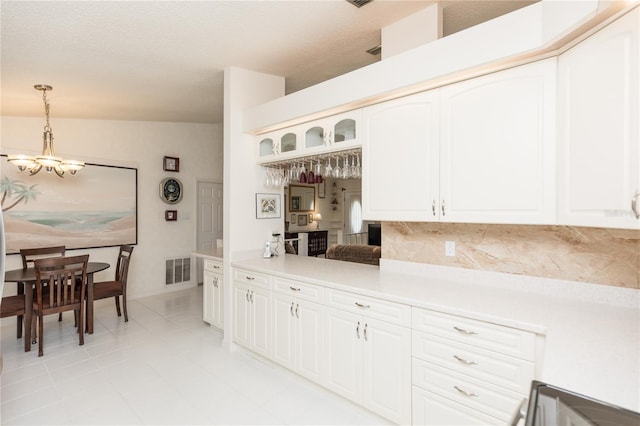 kitchen with visible vents, glass insert cabinets, pendant lighting, light countertops, and an inviting chandelier