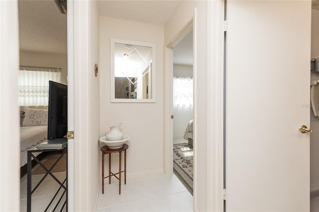 corridor with light tile patterned floors, baseboards, and a textured ceiling