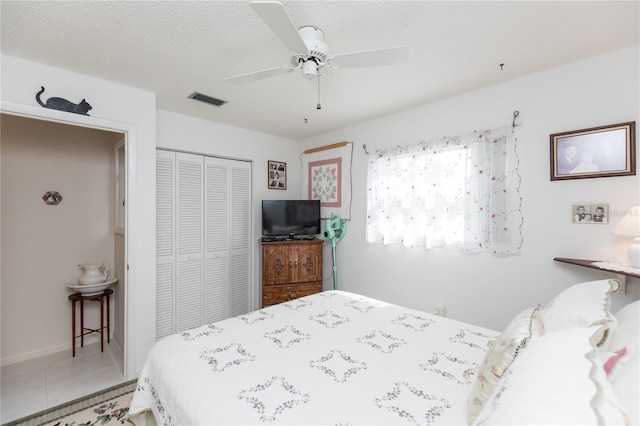 bedroom with visible vents, a textured ceiling, a closet, light tile patterned floors, and ceiling fan