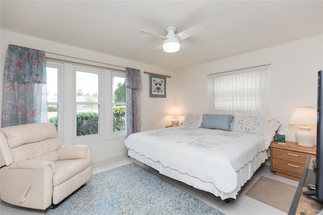 bedroom featuring light tile patterned floors, a ceiling fan, baseboards, and a textured ceiling