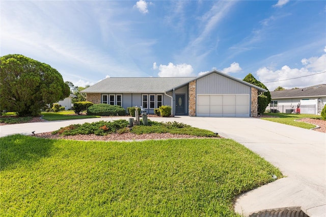 view of front of property featuring driveway, stone siding, fence, a front yard, and a garage