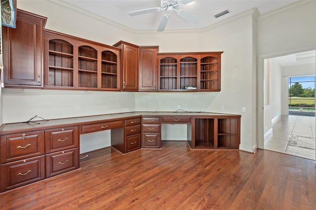 unfurnished office with ceiling fan, ornamental molding, dark hardwood / wood-style floors, and built in desk