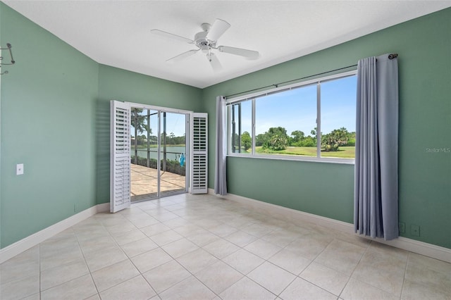 tiled empty room featuring a water view and ceiling fan