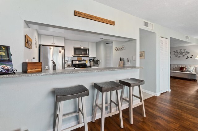 kitchen with kitchen peninsula, a kitchen breakfast bar, stainless steel appliances, dark hardwood / wood-style floors, and white cabinetry